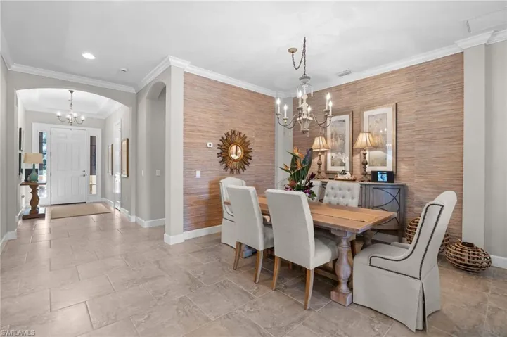 Dining area featuring hanging lights, an accent wall, arched walkways, and crown molding