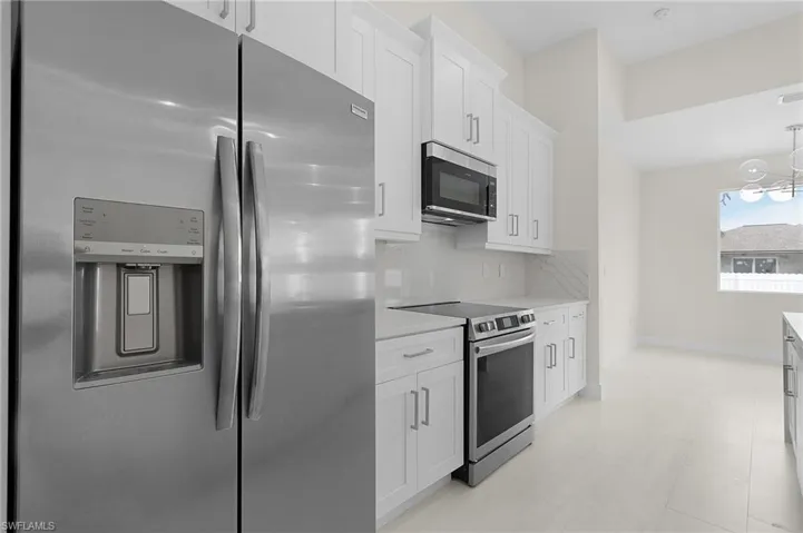 Kitchen with appliances with stainless steel finishes, white cabinets, decorative backsplash, pendant lighting, and light stone countertops