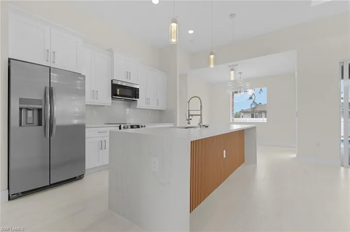 Kitchen featuring stainless steel appliances, white cabinetry, decorative backsplash, decorative light fixtures, and light stone countertops
