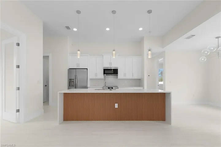 Kitchen featuring white cabinets, a large island with sink, stainless steel appliances, pendant lighting, and light stone counters