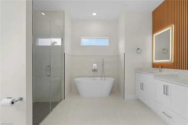 Full bath featuring a stall shower, a soaking tub, vanity, tile walls, and recessed lighting