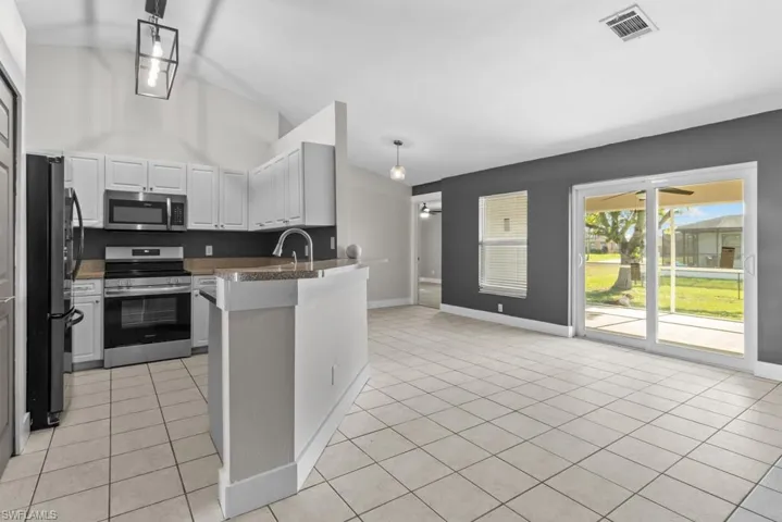 Kitchen with appliances with stainless steel finishes, a peninsula, light tile patterned flooring, baseboards, and high vaulted ceiling