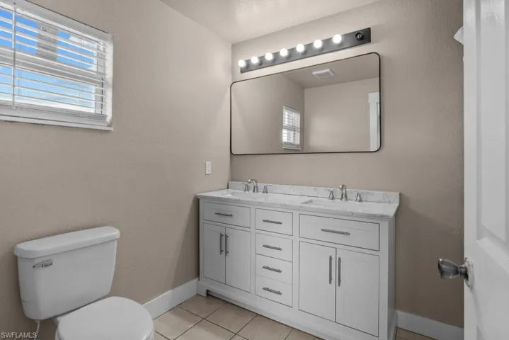 Full bath with toilet, tile patterned flooring, double vanity, and baseboards