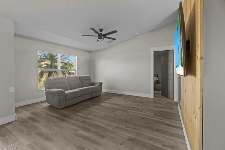 Living room featuring a ceiling fan, wood finished floors, vaulted ceiling, and baseboards