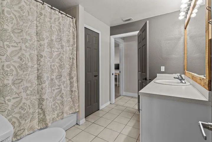 Bathroom with tile patterned flooring, toilet, a textured ceiling, vanity, and shower / bath combo with shower curtain