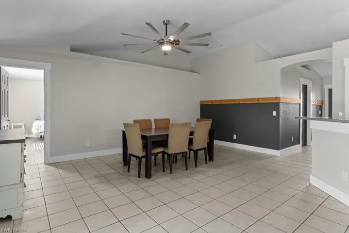 Dining space featuring lofted ceiling, ceiling fan, baseboards, arched walkways, and light tile patterned flooring