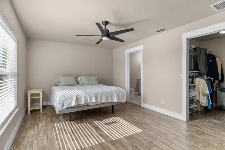 Bedroom featuring wood finished floors, a walk in closet, baseboards, and ensuite bath
