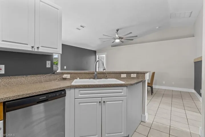 Kitchen featuring stainless steel dishwasher, a sink, vaulted ceiling, a peninsula, and white cabinets