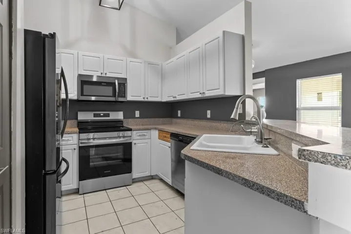 Kitchen with stainless steel appliances, a sink, white cabinets, light tile patterned flooring, and a peninsula