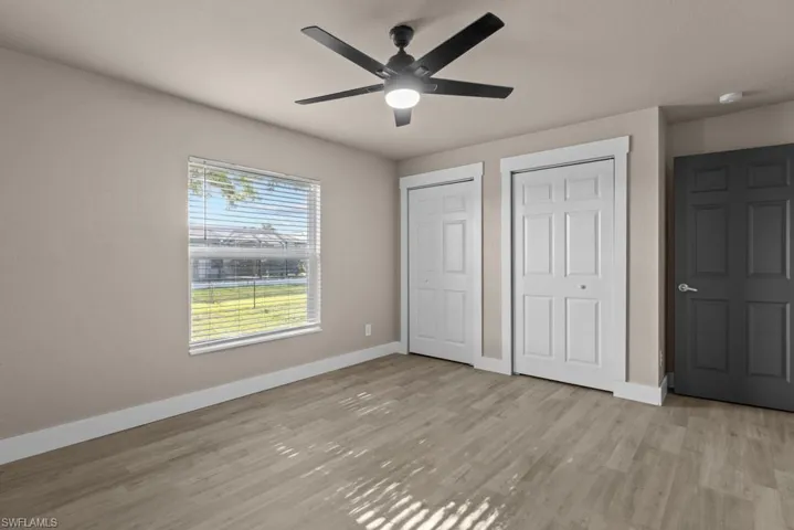 Unfurnished bedroom with multiple closets, baseboards, light wood-style floors, and ceiling fan