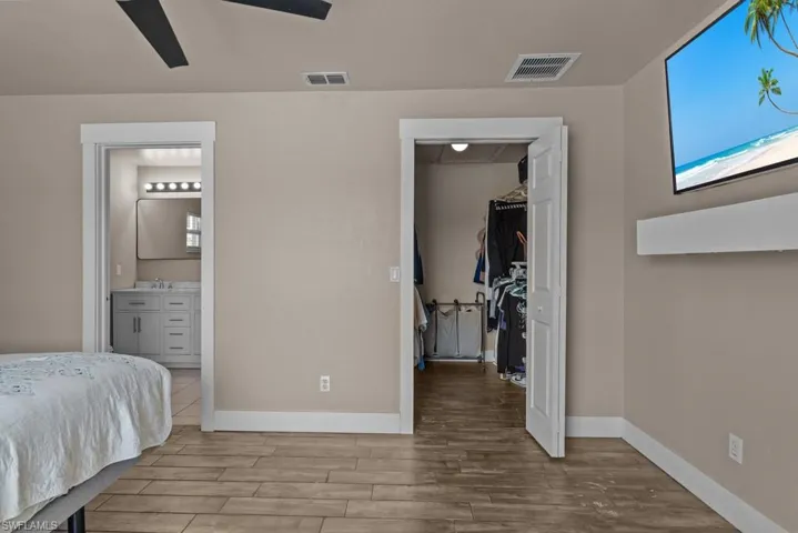 Bedroom featuring a walk in closet, wood finished floors, baseboards, and ensuite bathroom