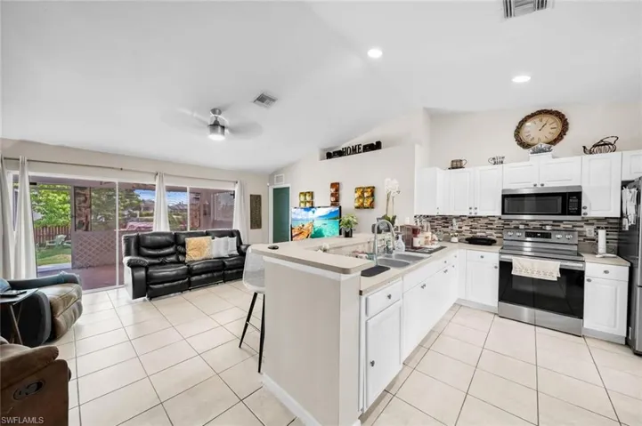 Kitchen with kitchen peninsula, appliances with stainless steel finishes, sink, white cabinetry, and lofted ceiling