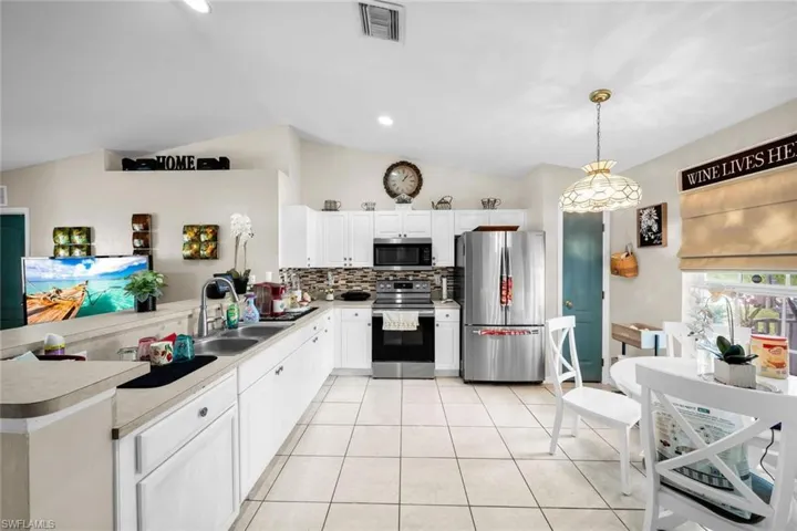 Kitchen with hanging light fixtures, sink, vaulted ceiling, appliances with stainless steel finishes, and white cabinetry