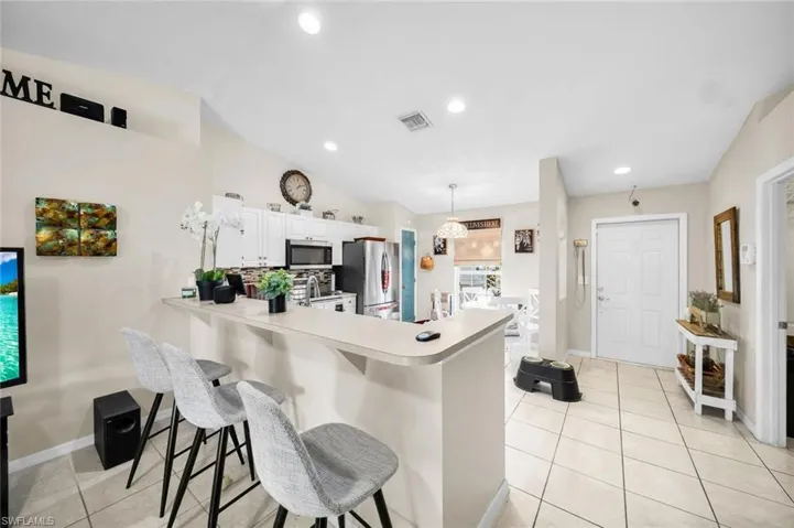Kitchen with hanging light fixtures, kitchen peninsula, a breakfast bar, white cabinets, and appliances with stainless steel finishes