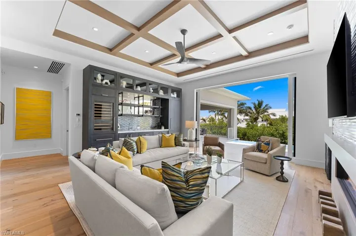 Living area with coffered ceiling, light wood-style floors, baseboards, a lit fireplace, and beam ceiling