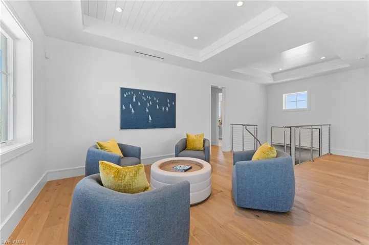 Living area with a tray ceiling, an upstairs landing, wood finished floors, recessed lighting, and baseboards