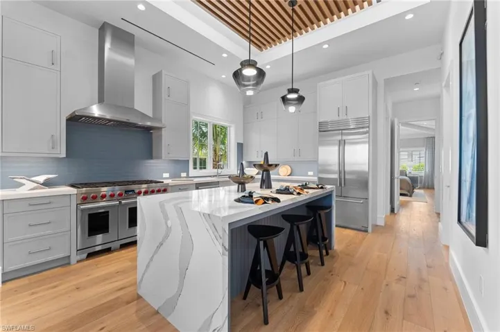 Kitchen with premium appliances, wall chimney exhaust hood, a center island, light stone countertops, and light wood-style floors