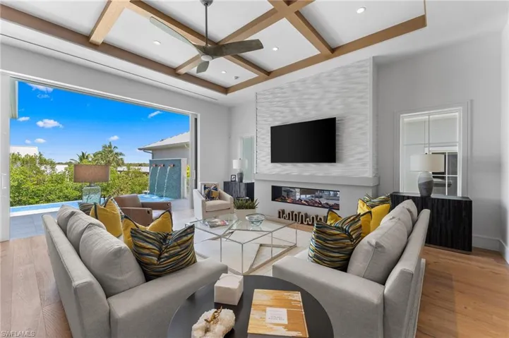 Living area featuring coffered ceiling, wood finished floors, a glass covered fireplace, ceiling fan, and beam ceiling