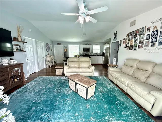 Living room with vaulted ceiling, a ceiling fan, and dark wood-style floors