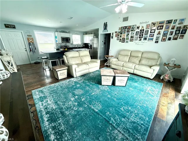 Living room with a ceiling fan, dark wood-type flooring, and lofted ceiling