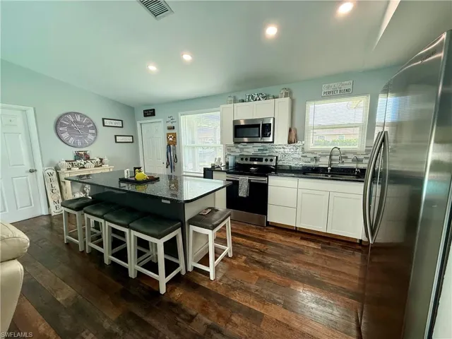Kitchen featuring stainless steel appliances, lofted ceiling, tasteful backsplash, healthy amount of natural light, and dark wood-style floors