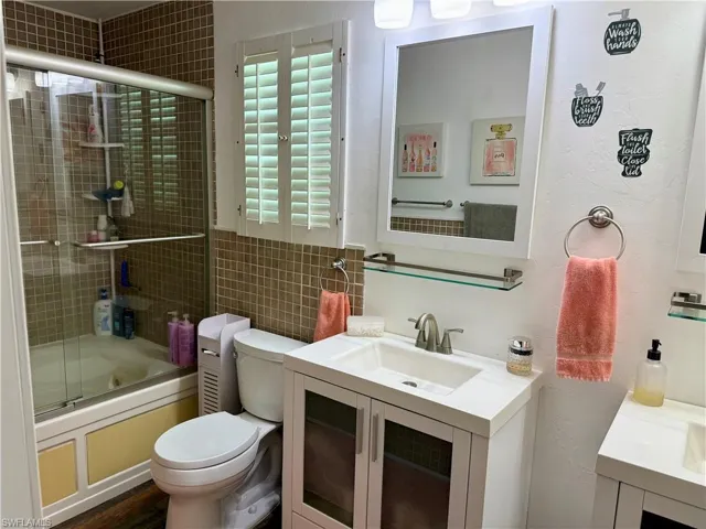 Full bath featuring vanity, bath / shower combo with glass door, and tile walls