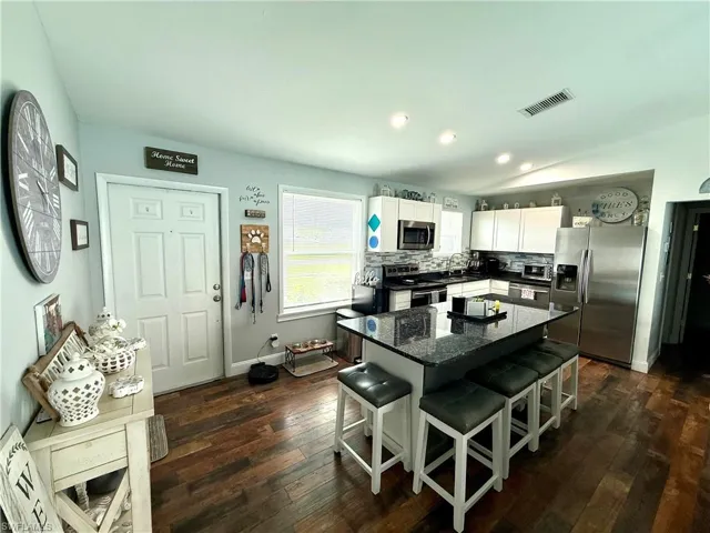 Kitchen with stainless steel appliances, a kitchen bar, dark wood finished floors, white cabinets, and recessed lighting