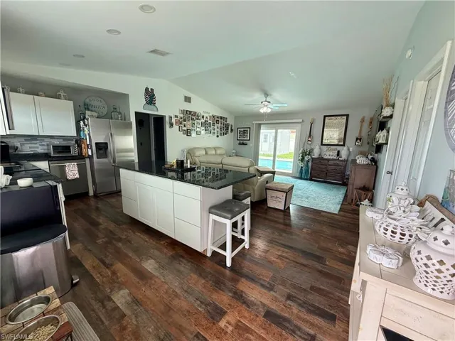 Kitchen with stainless steel appliances, dark countertops, vaulted ceiling, a center island, and open floor plan