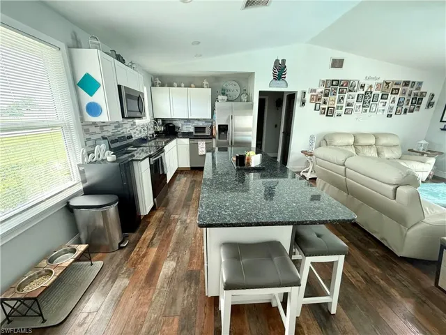 Kitchen with appliances with stainless steel finishes, lofted ceiling, open floor plan, healthy amount of natural light, and dark wood finished floors