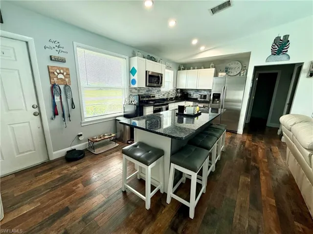 Kitchen with appliances with stainless steel finishes, a kitchen bar, dark wood-style floors, white cabinetry, and a kitchen island