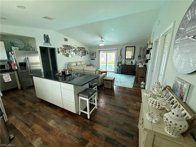Kitchen featuring stainless steel fridge with ice dispenser, vaulted ceiling, dark wood-style flooring, a center island, and white cabinetry