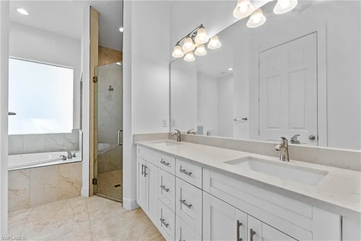 Bathroom featuring a stall shower, a garden tub, double vanity, a chandelier, and recessed lighting