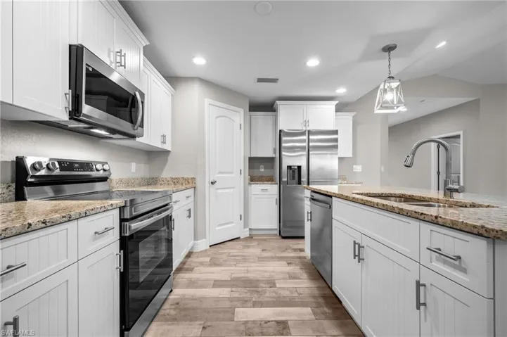 Kitchen featuring white cabinetry, stainless steel appliances, granite countertops, wood-finish flooring, and recessed lighting