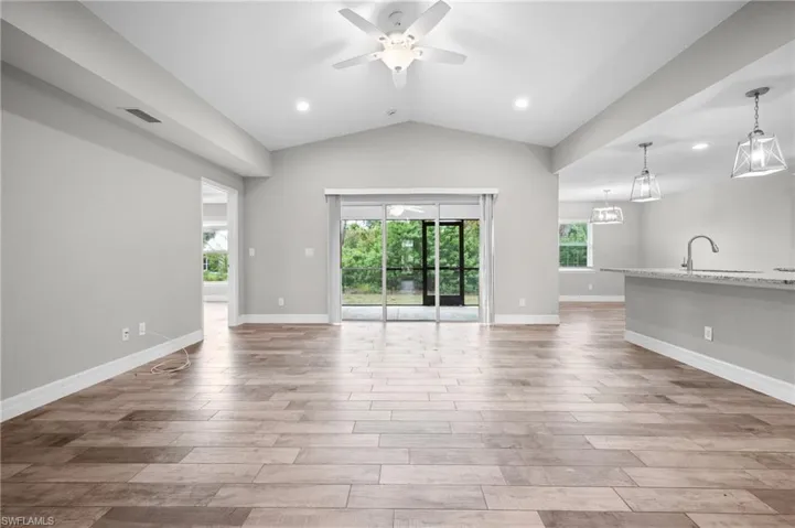 Vaulted ceiling with a ceiling fan and recessed lighting, wood-finish flooring, sliding glass doors, and a kitchen island with pendant lighting and a stainless steel faucet