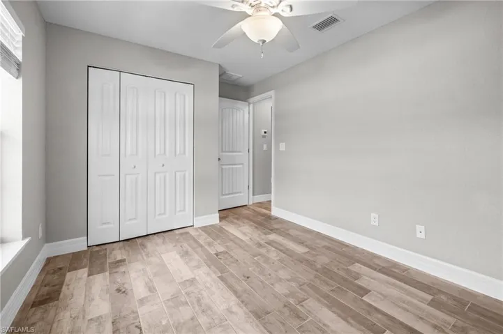 Wood-finish flooring, white bi-fold closet doors, ceiling fan, and light gray wall paint