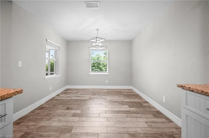 Bright, open room featuring wood-finish plank flooring, clean white walls, and abundant natural light from dual windows