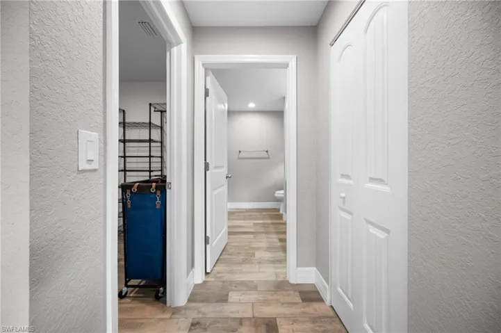 Hallway featuring wood-finish flooring, white paneled doors, and light gray wall texture