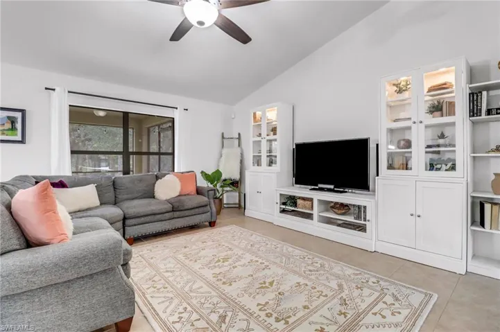 Living room with ceiling fan, tile patterned flooring, and vaulted ceiling