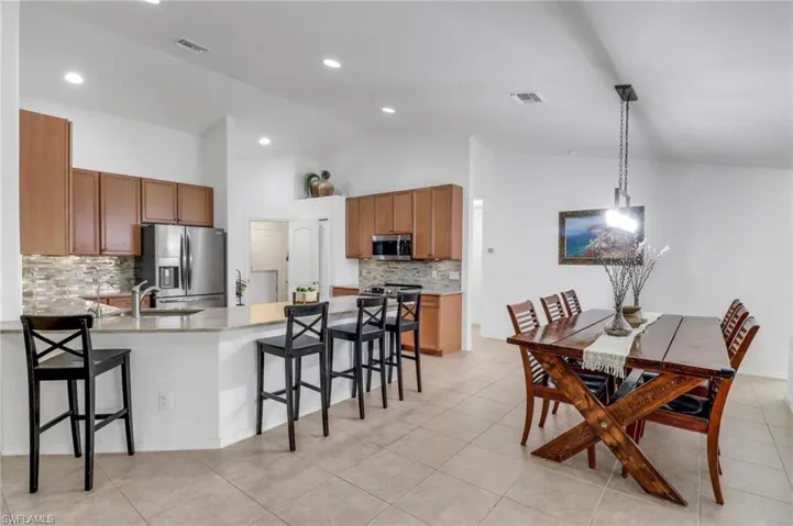 Kitchen featuring stainless steel appliances, decorative backsplash, decorative light fixtures, and a kitchen bar