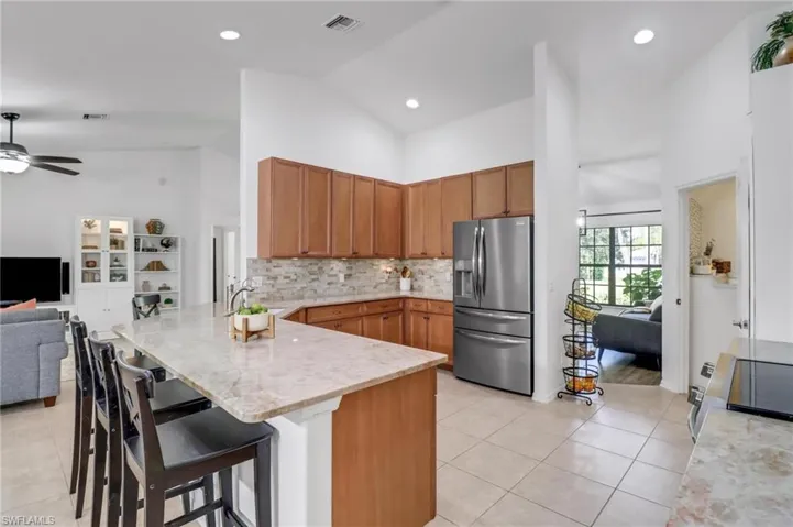 Kitchen featuring light tile patterned flooring, kitchen peninsula, high vaulted ceiling, stainless steel appliances, and a breakfast bar area