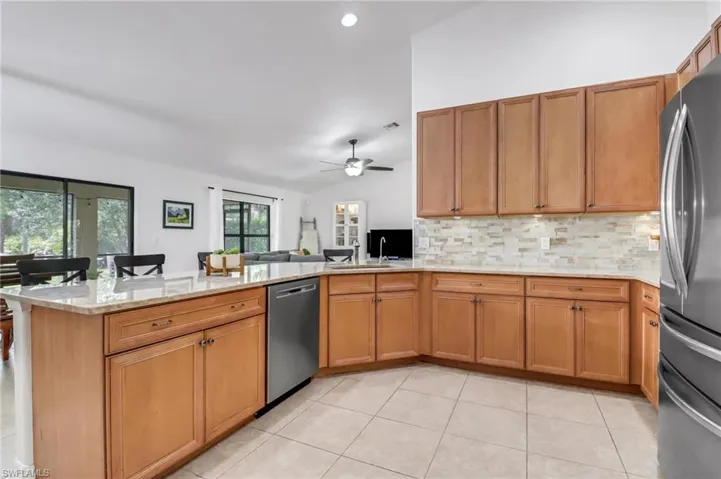 Kitchen featuring ceiling fan, light tile patterned floors, kitchen peninsula, backsplash, and stainless steel appliances