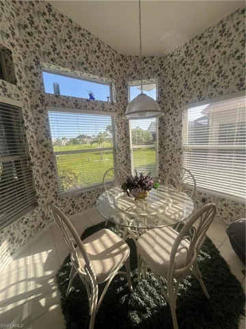Breakfast nook featuring multiple windows with horizontal blinds, patterned wallpaper, and a hanging pendant light fixture