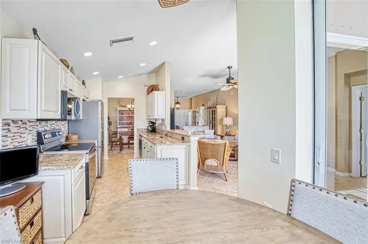 Kitchen with stainless steel appliances, white cabinets, light stone counters, vaulted ceiling, and recessed lighting