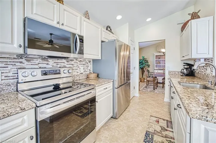 Kitchen with stainless steel appliances, light stone countertops, white cabinets, tasteful backsplash, and lofted ceiling