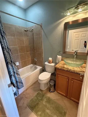 Bathroom with a textured wall, shower / tub combo with curtain, vanity, and light tile patterned floors