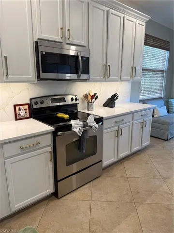 Kitchen featuring stainless steel range with electric stovetop, light tile patterned floors, tasteful backsplash, light stone countertops, and crown molding