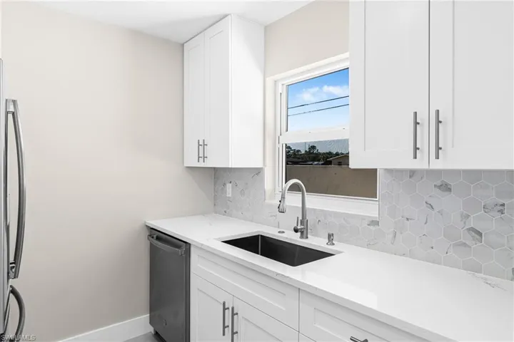 Kitchen with decorative backsplash, white cabinets, appliances with stainless steel finishes, and light stone counters