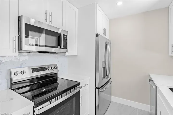 Kitchen with appliances with stainless steel finishes, white cabinetry, backsplash, light stone countertops, and recessed lighting
