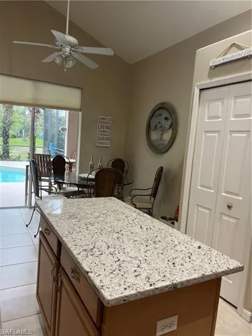 Kitchen featuring light stone counters, a center island, light tile patterned floors, vaulted ceiling, and a ceiling fan