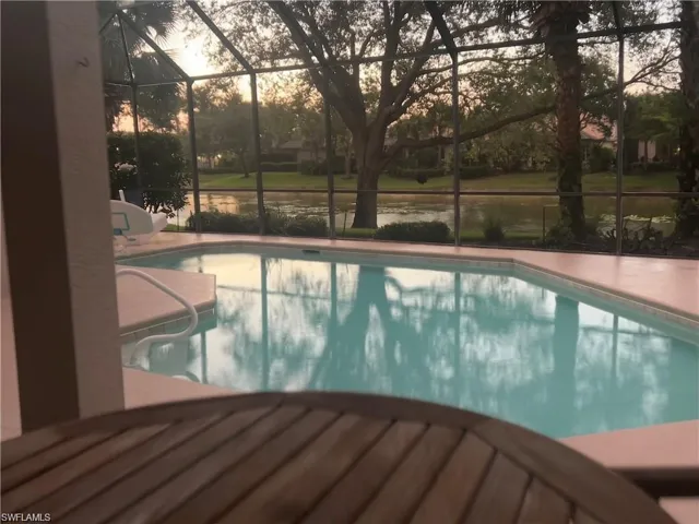 Pool at dusk featuring an outdoor pool, a sunroom, and a water view